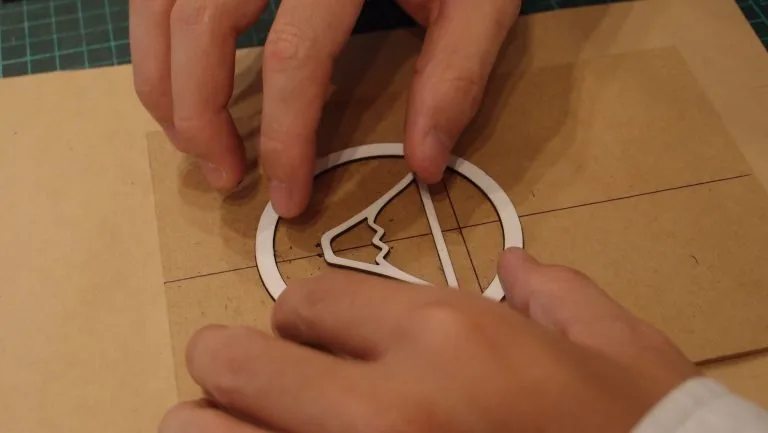 Hands arranging a paper prototype for a circular notebook-cover pattern