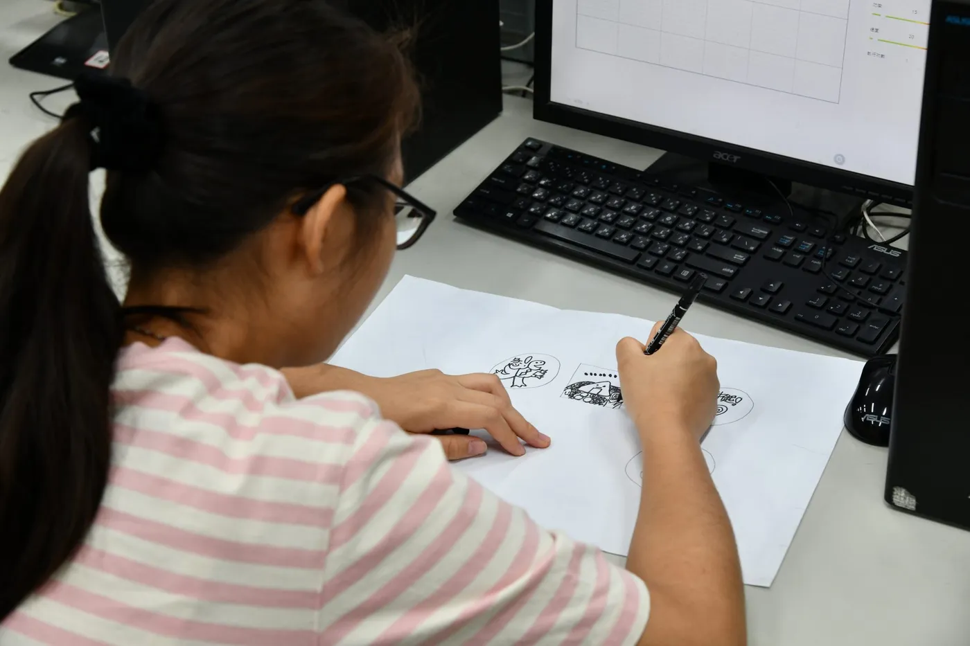 A student sketching a design beside a classroom computer