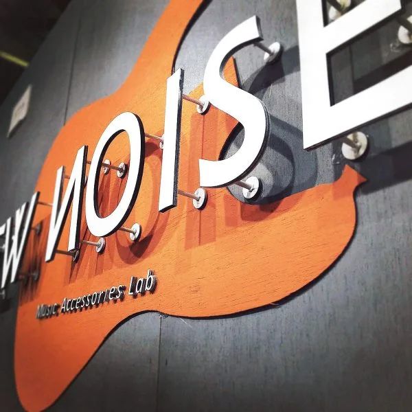 Layered New Noise shop lettering mounted over a guitar silhouette
